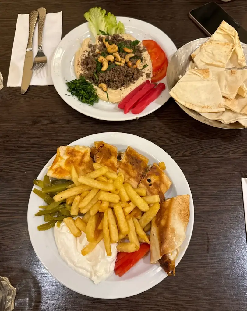 Zwei Teller mit Grillspezialitäten, Pommes und Fladenbrot auf Holztisch