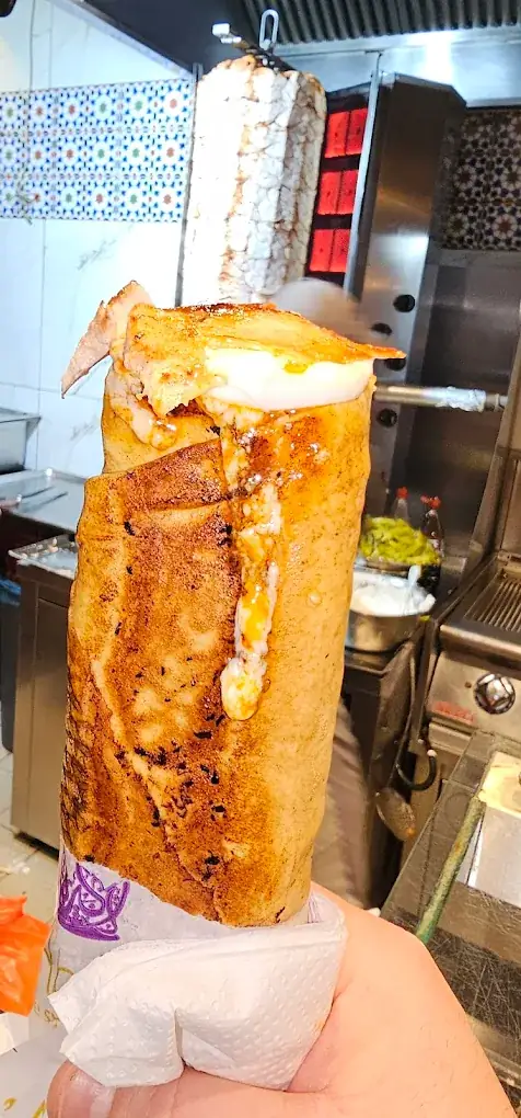 Frisch gewickelter, goldbraun gegrillter Schawarma-Wrap in der Hand vor dem Drehspieß